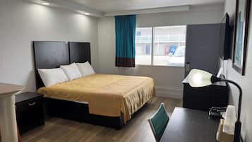 Ett hotellrum med en säng, ett nattduksbord, ett skrivbord med en lampa och ett fönster med gardiner.