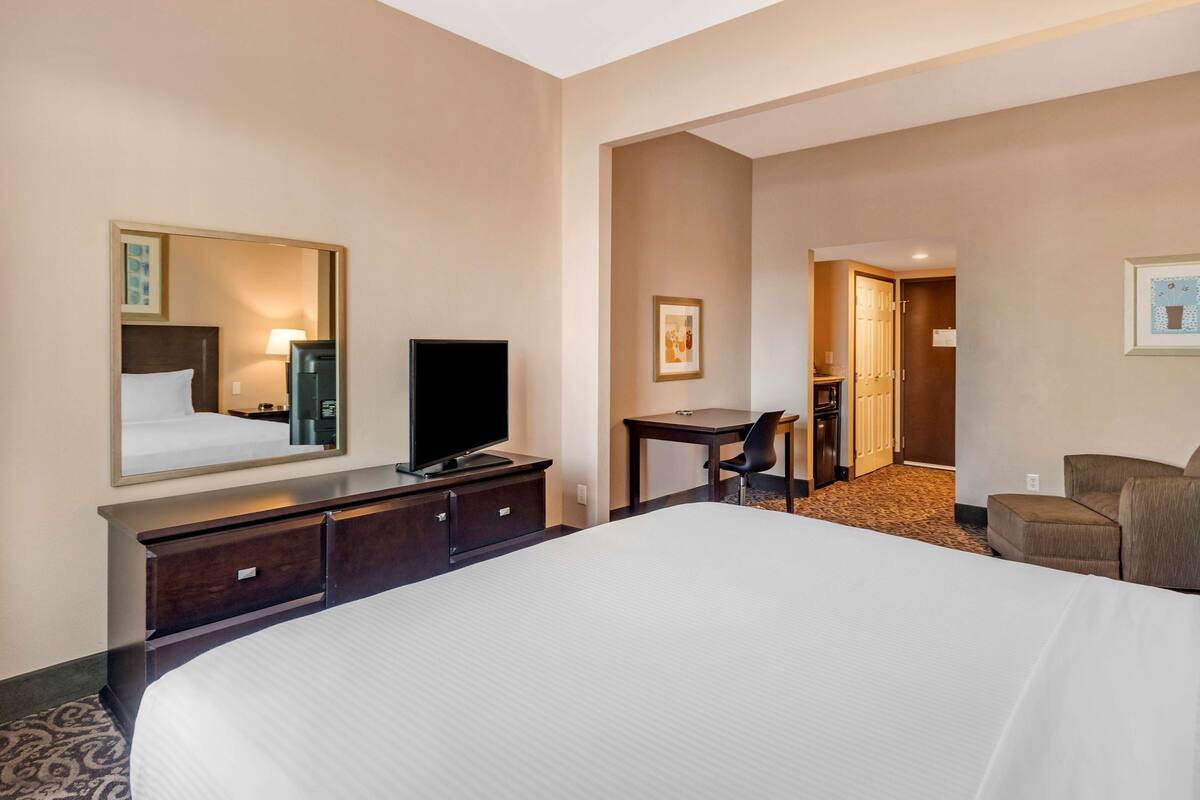 Ein Hotelzimmer mit einem großen Bett, einem Schreibtisch, einem Stuhl, einem Fernseher und einem Spiegel.