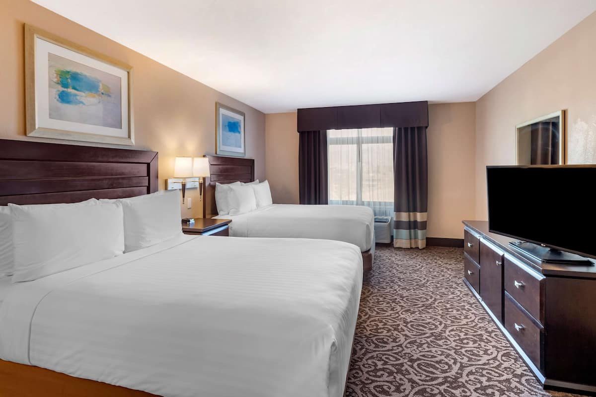 Habitación de hotel con dos camas, un televisor de pantalla plana, un aparador y una ventana con cortinas.