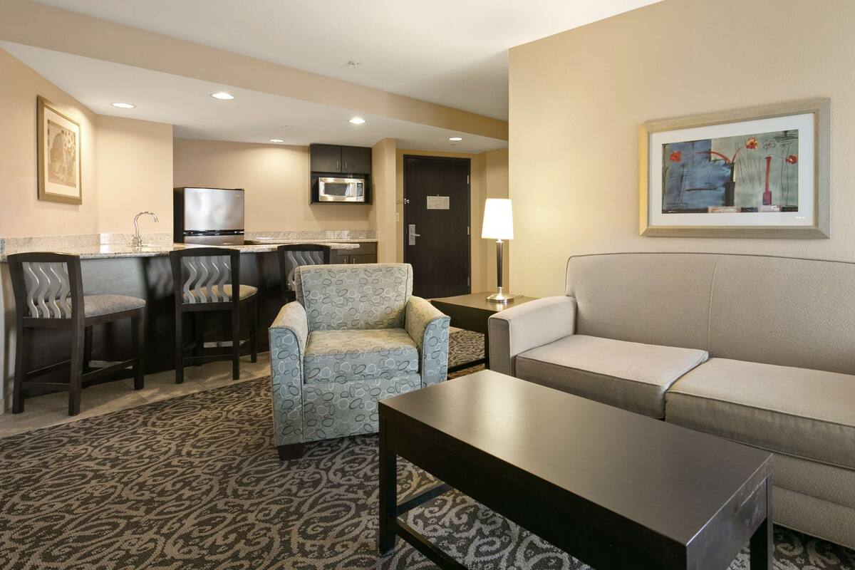 Ein Hotelzimmer mit Sofa, Sesseln, Couchtisch, Fernseher, Mikrowelle und einem Gemälde an der Wand.