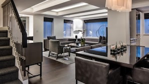 A modern living room with a staircase, a dining area, and large windows.