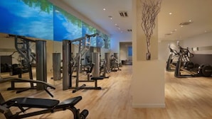 A gym with various exercise equipment, a wooden floor, and a wall with a blue sky mural.