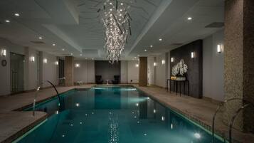 An indoor swimming pool with a modern chandelier, seating area, and a brick accent wall.