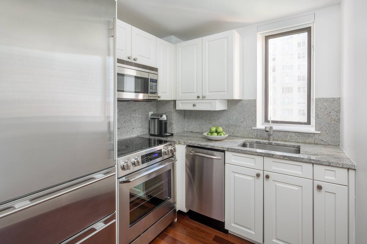 A modern kitchen with stainless steel appliances, white cabinetry, and a window providing natural light.