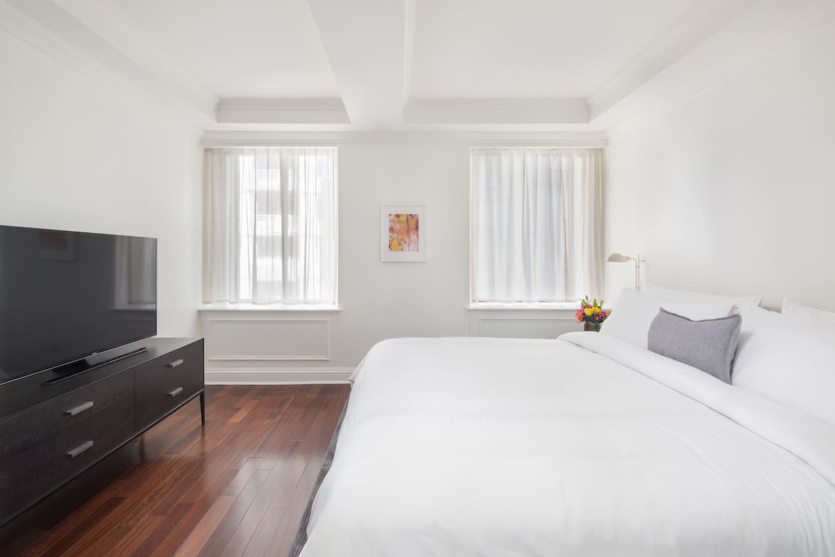 A modern hotel room with a large bed, a flat-screen TV, and a wooden floor.