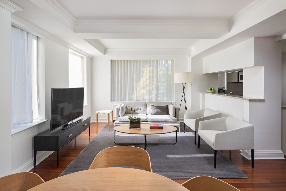 A modern living room with a flat-screen TV, a sofa, a coffee table, and a dining area.