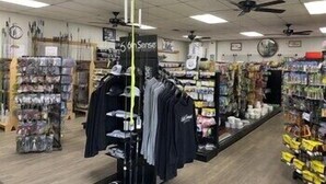 Interior de loja de roupas com araras, um manequim e diversos itens nas prateleiras.