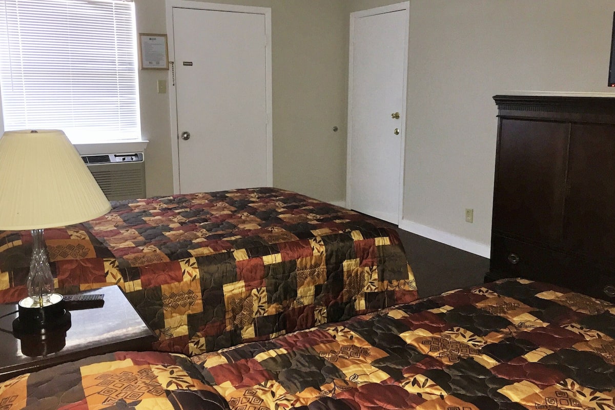 A bedroom with two beds, a lamp, a dresser, and a window with blinds.
