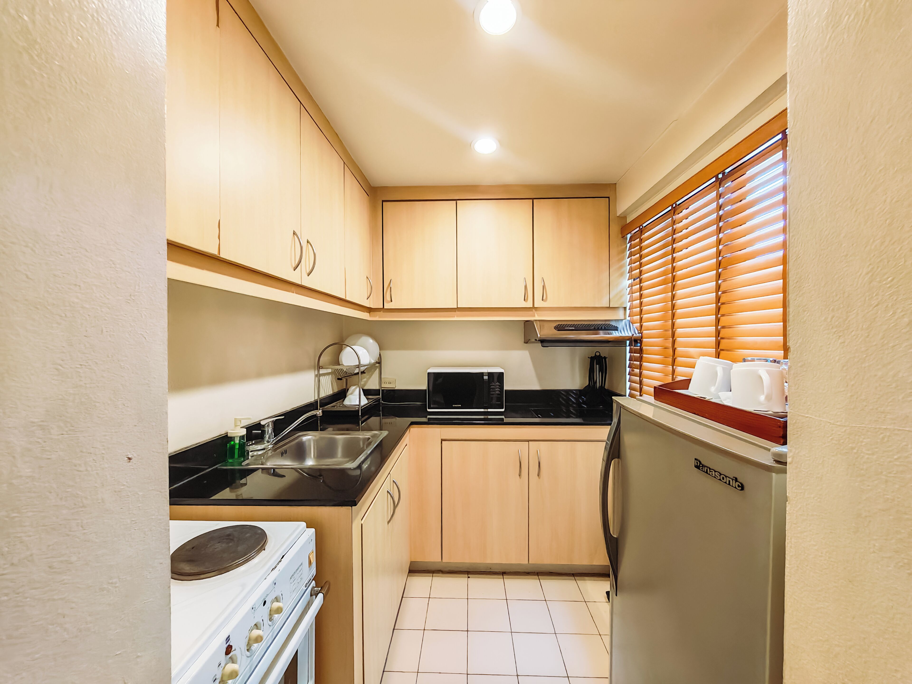 Cocina compacta con armarios de madera, microondas, fregadero y estufa.