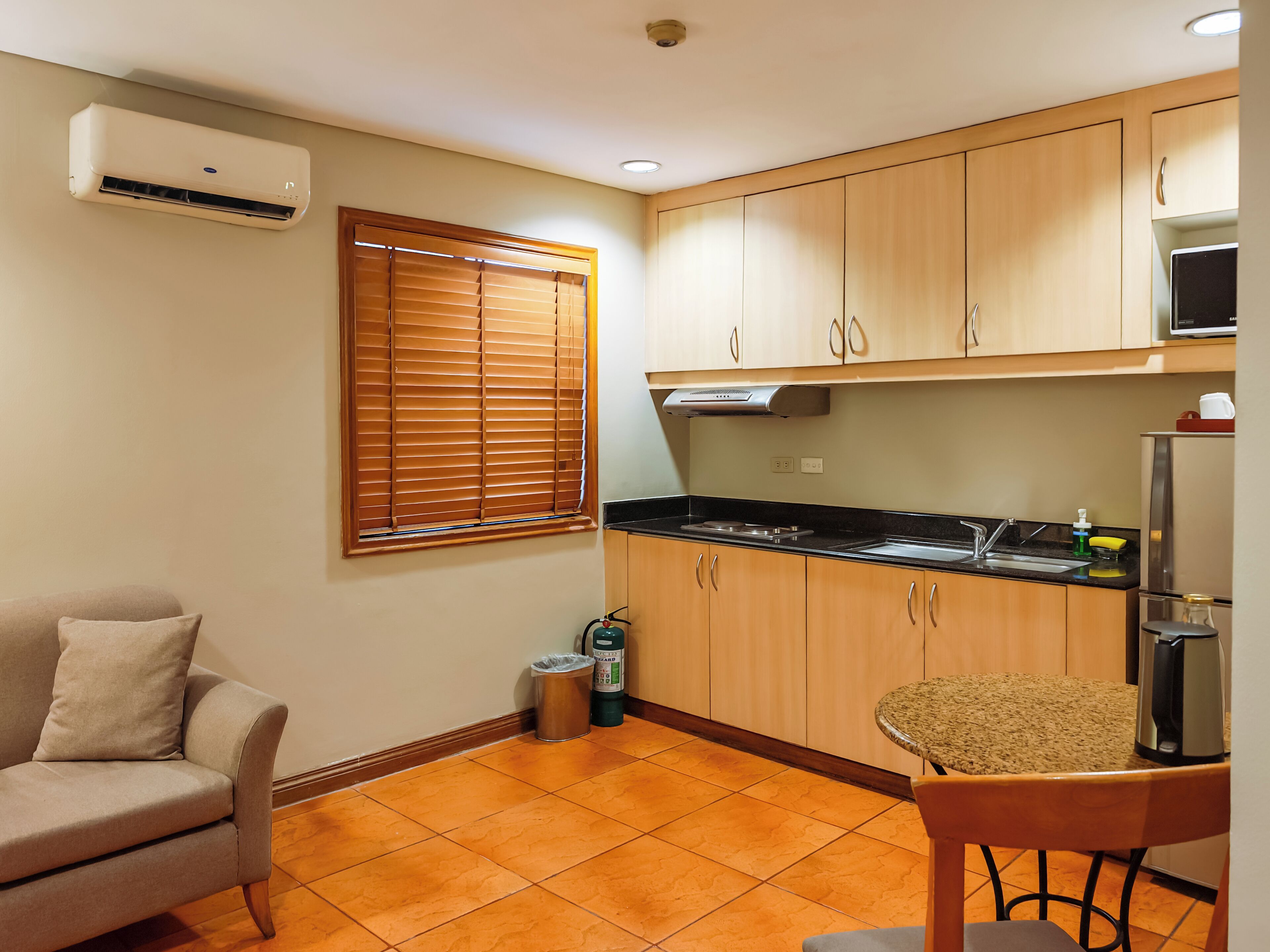 Cocina compacta con armarios de madera, estufa integrada y un pequeño comedor con una silla.