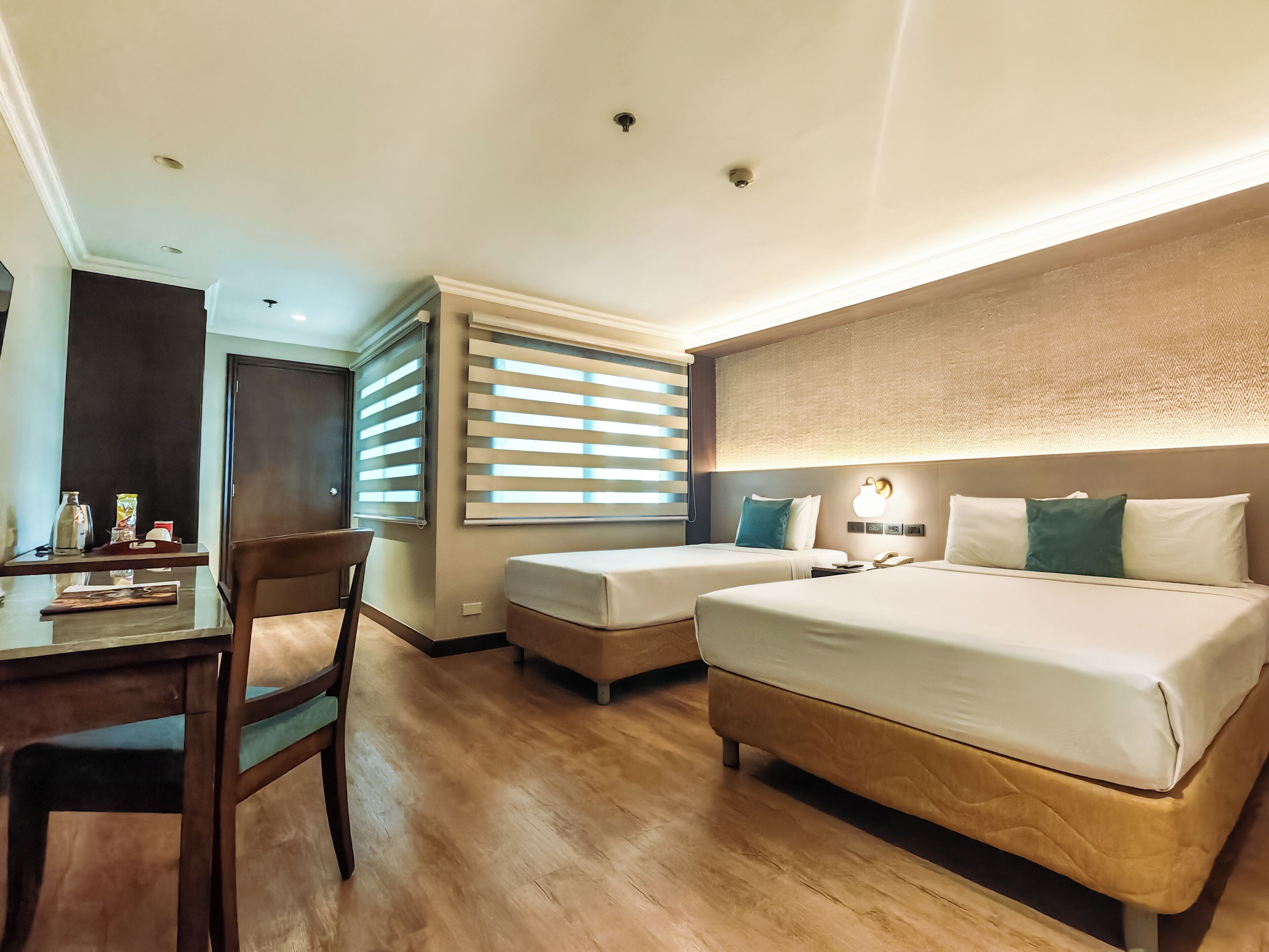 A hotel room with a bed, a desk, a chair, and a window with blinds.