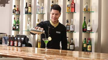 Un barman servint una beguda en un vas de martini a un bar, amb diverses ampolles de licors al fons.
