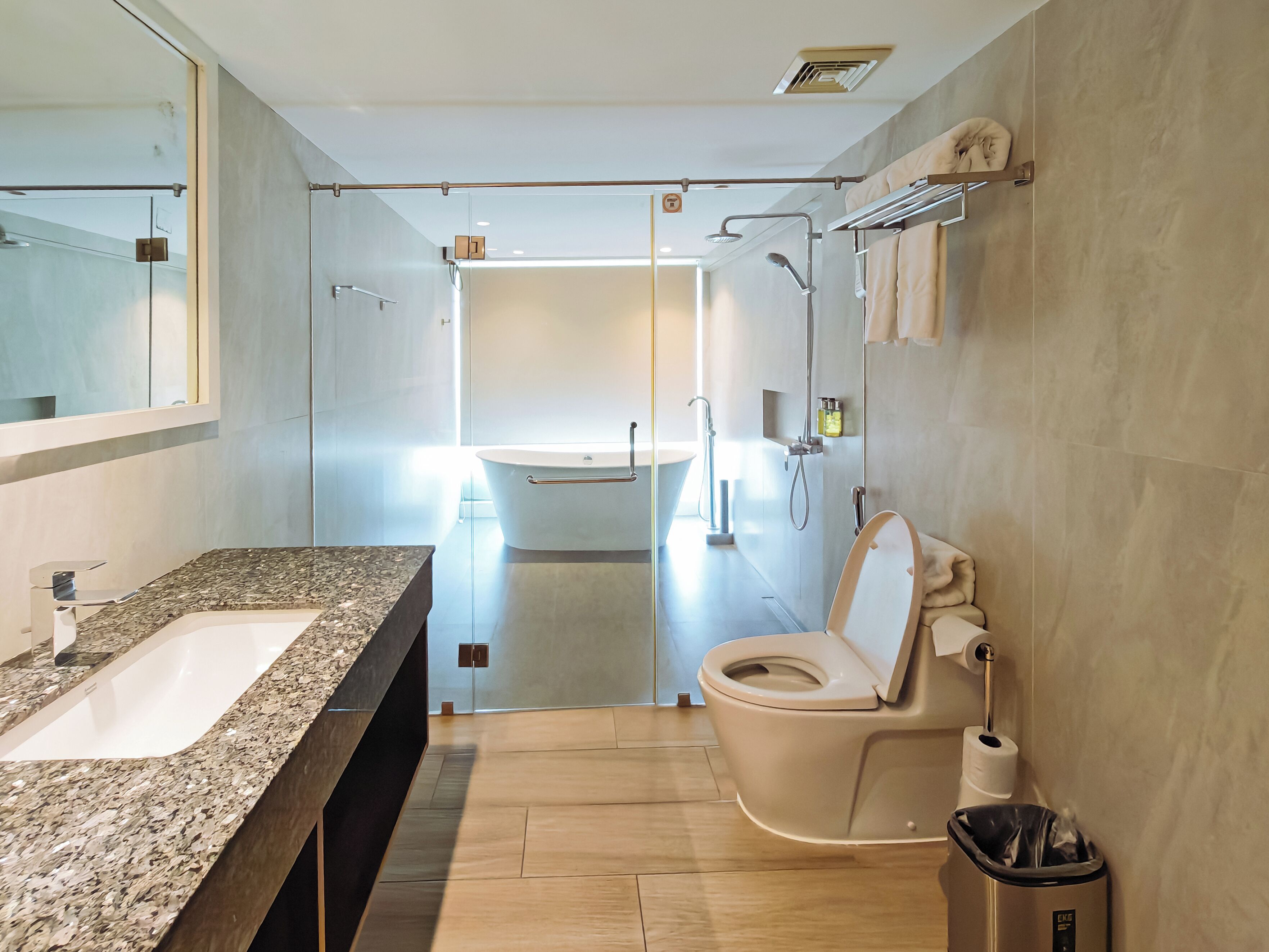 A modern bathroom with a granite countertop, a toilet, a shower, and a sink.