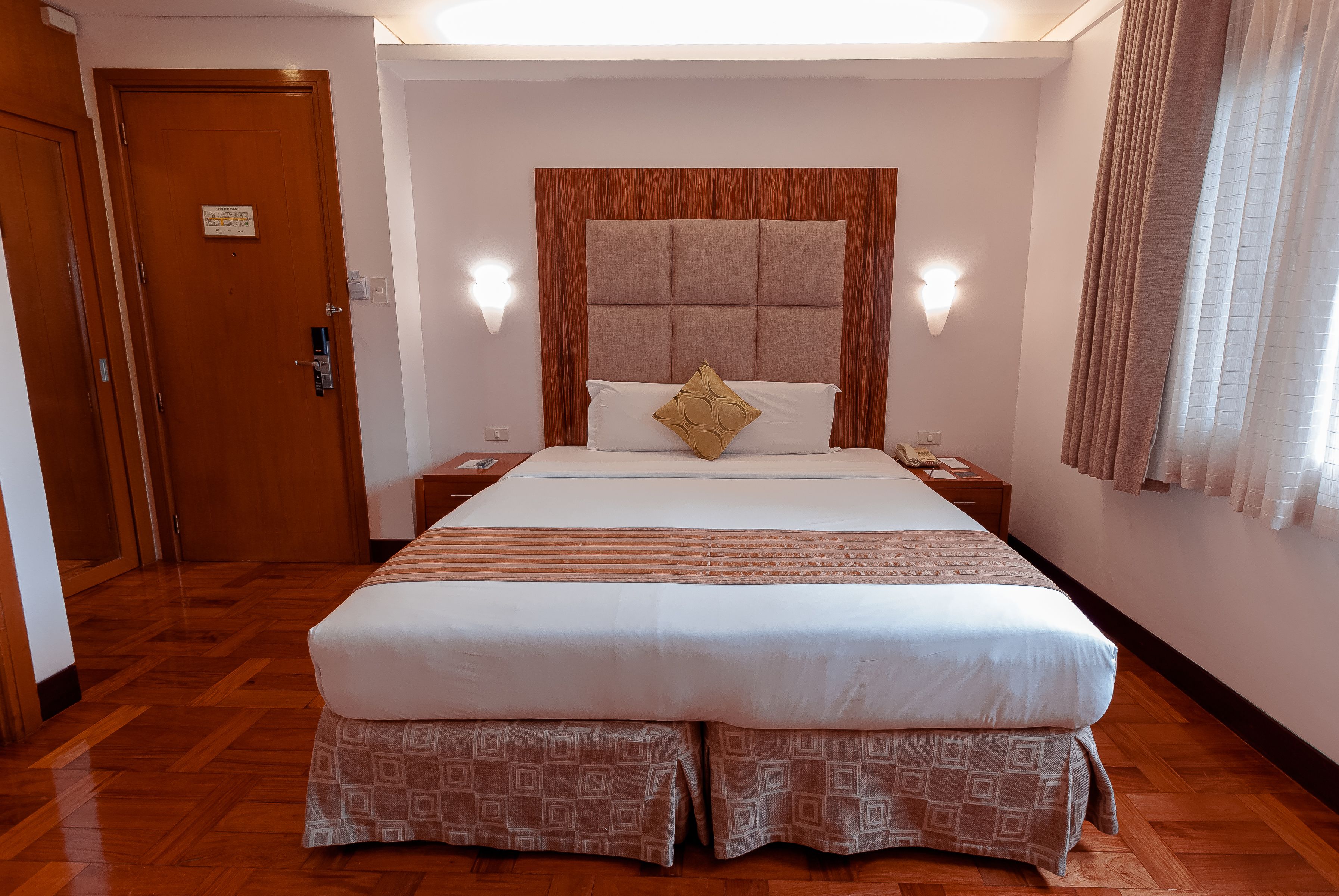 Una habitación de hotel con una cama grande, cabecero de madera, mesitas de noche y una puerta.