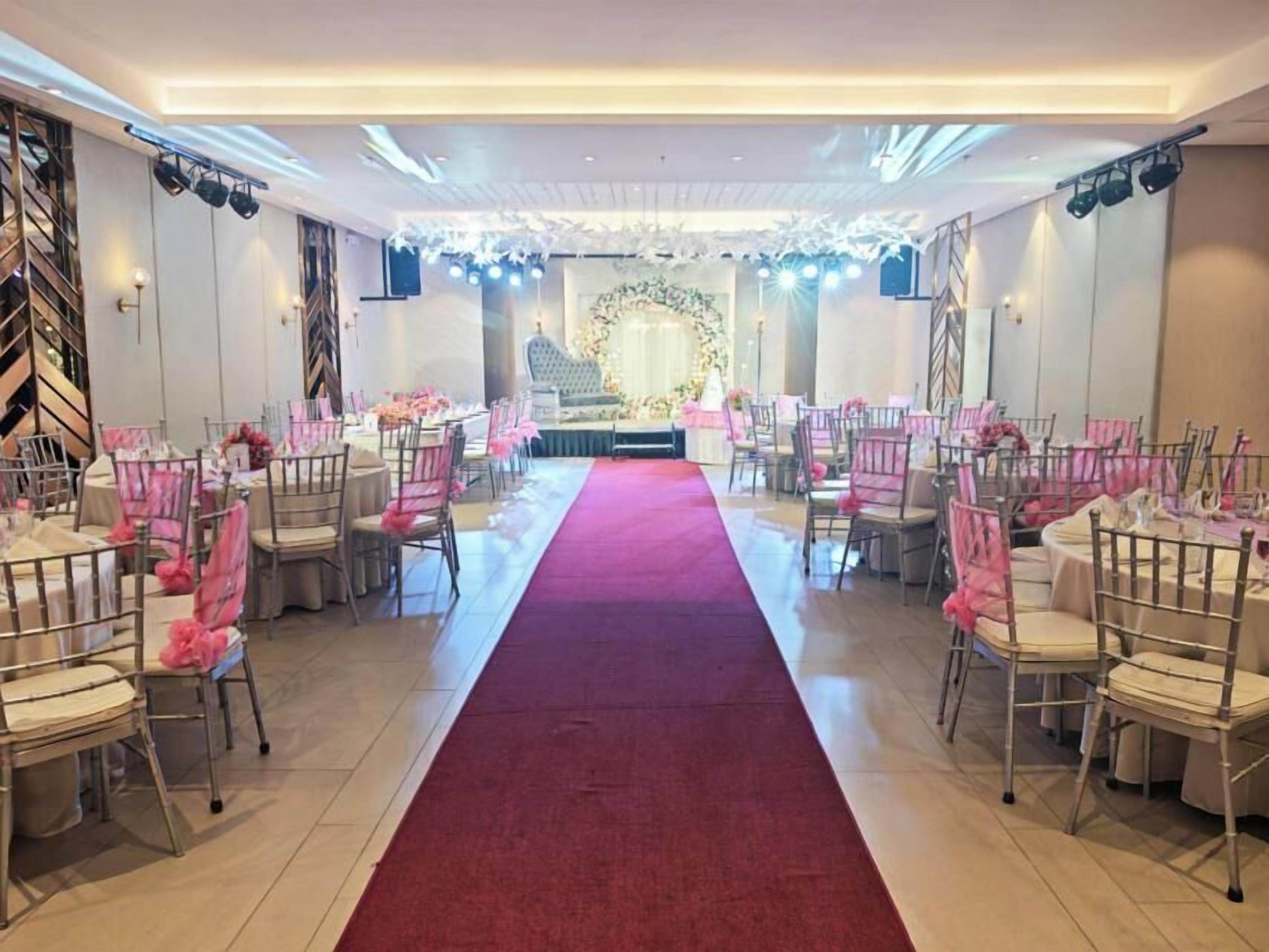 Uma sala de banquetes com um corredor central, fileiras de mesas e cadeiras.