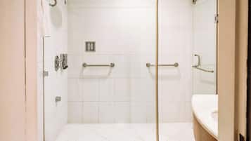 A glass-enclosed shower with a handrail, a white tiled wall, and a visible control panel.