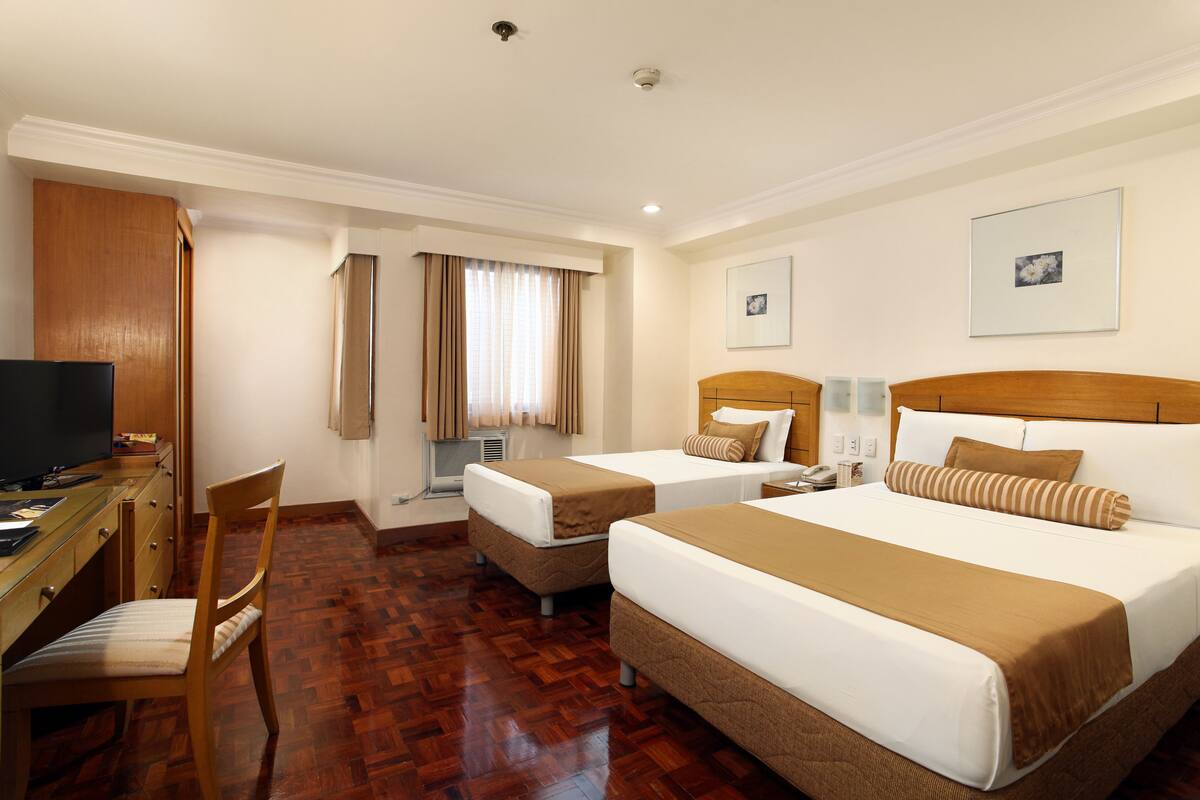 A hotel room with two beds, a desk with a computer, a chair, and a television.