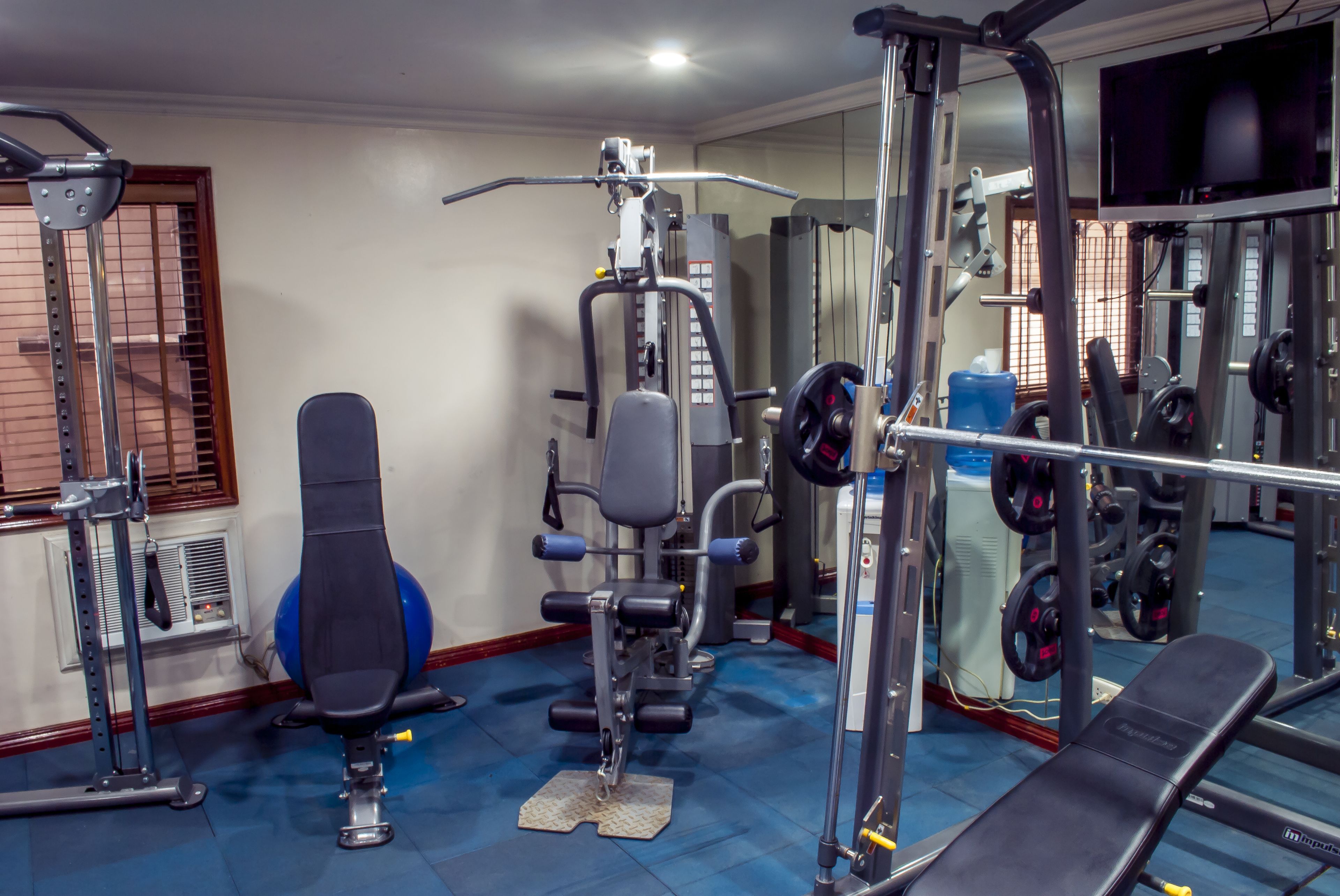 A gym with exercise equipment, a bench, and a mirrored wall.