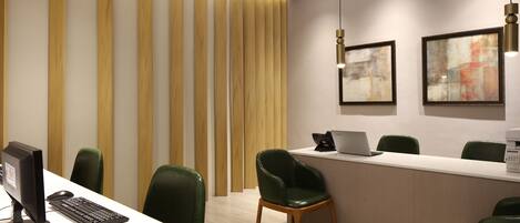 A modern reception desk with a computer, chairs, and artwork on the wall.