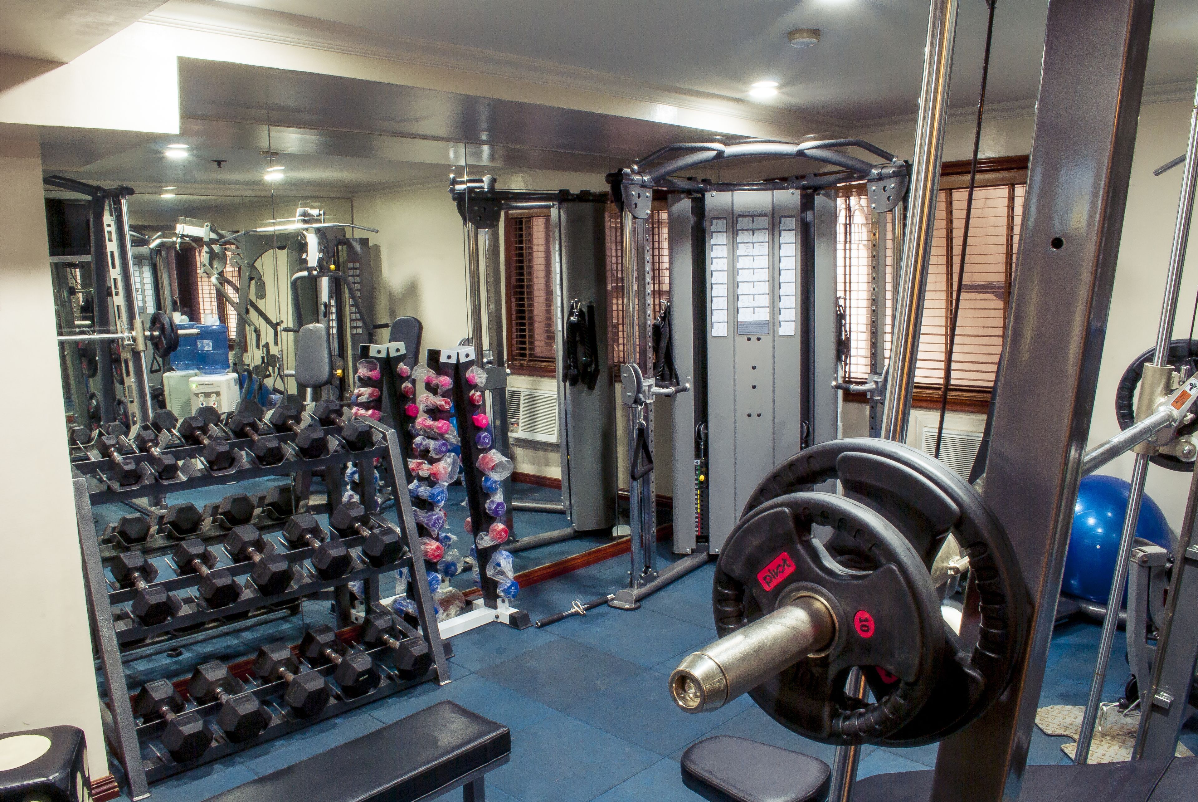 Un gimnasio con varios equipos de ejercicio, incluyendo mancuernas, una jaula para sentadillas y una banca.