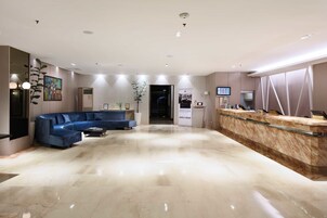 A modern hotel lobby with a marble floor, a blue sofa, a reception desk, and a large painting on the wall.