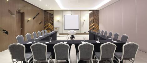 A conference room with a long table, grey chairs, and a projector screen.