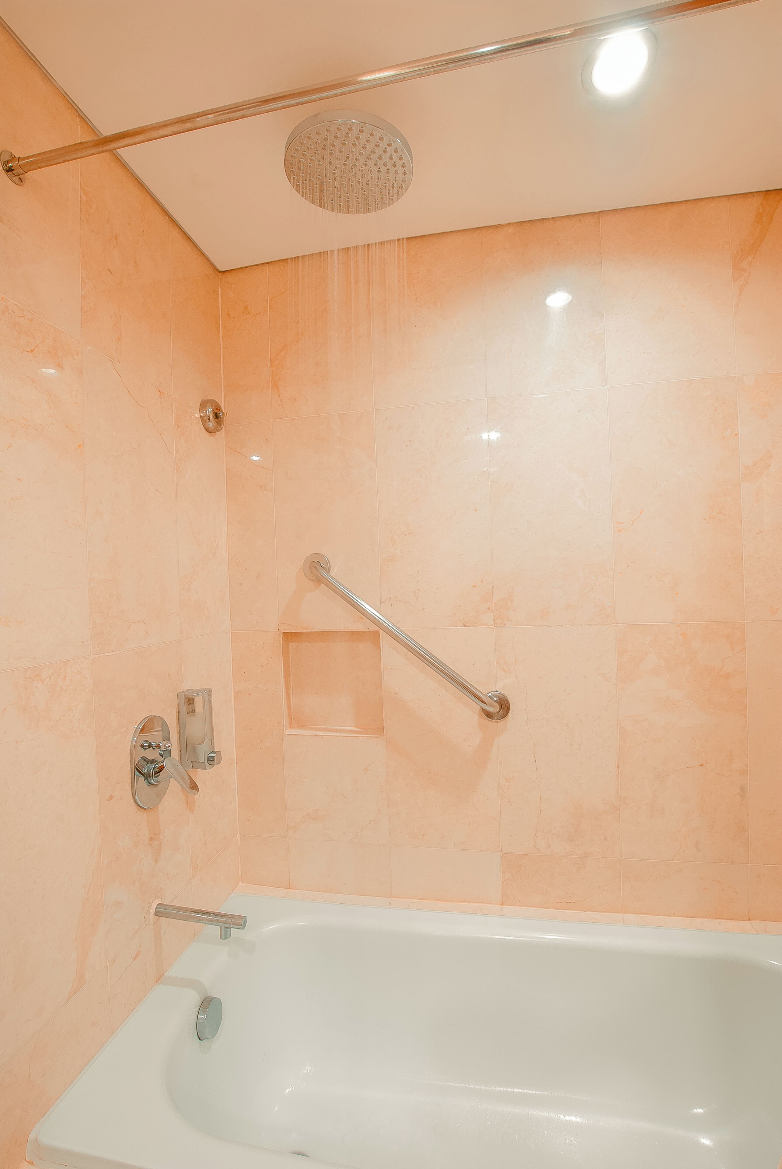 A bathroom with a bathtub, a shower head, and a handrail.