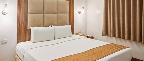 A hotel room with a large bed, a wooden headboard, a bedside table with a lamp, and a window with curtains.