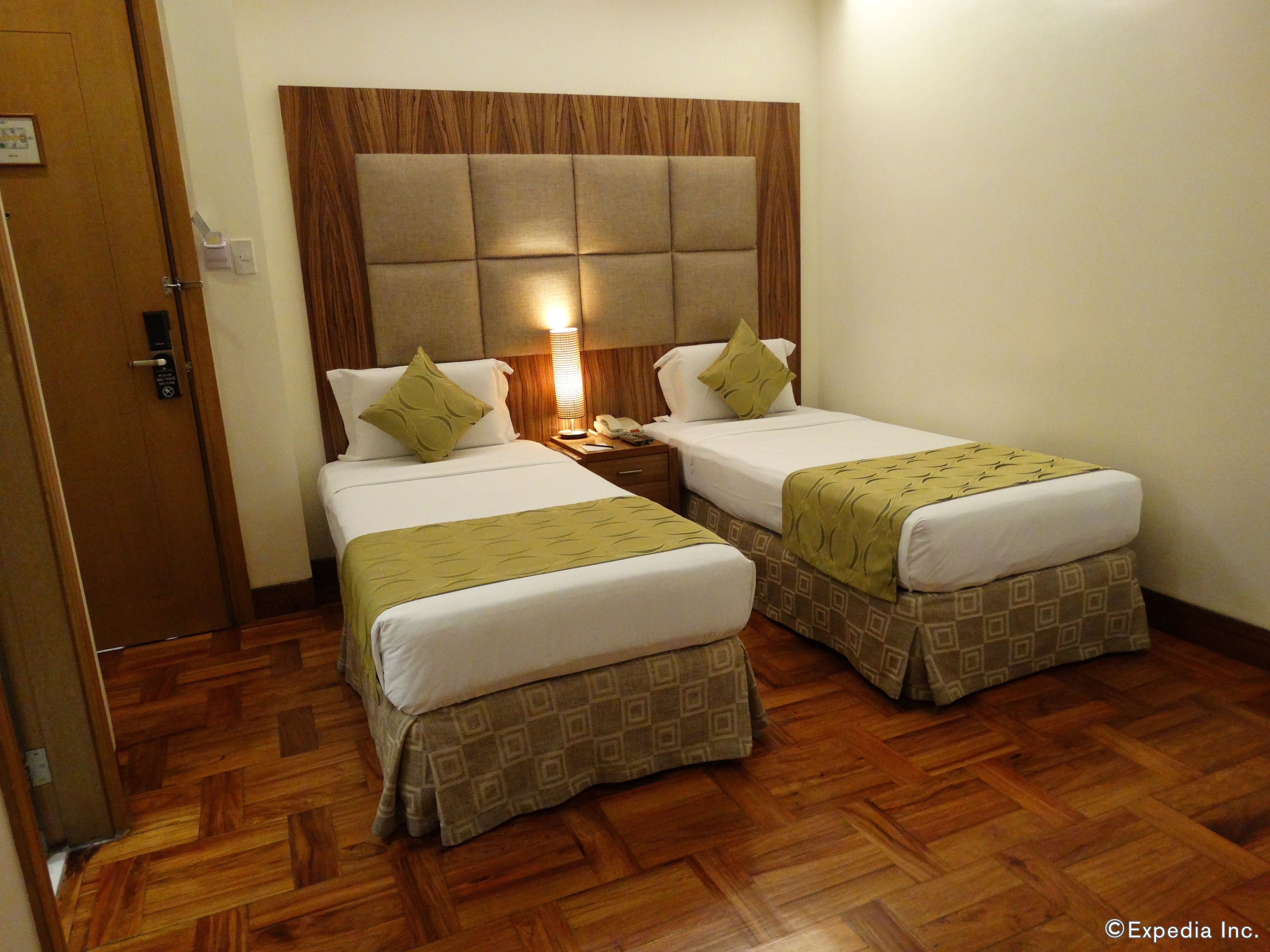 A hotel room with two beds, a wooden headboard, a bedside lamp, and a wooden floor.