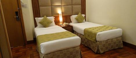 A hotel room with two beds, a wooden headboard, a bedside lamp, and a wooden floor.