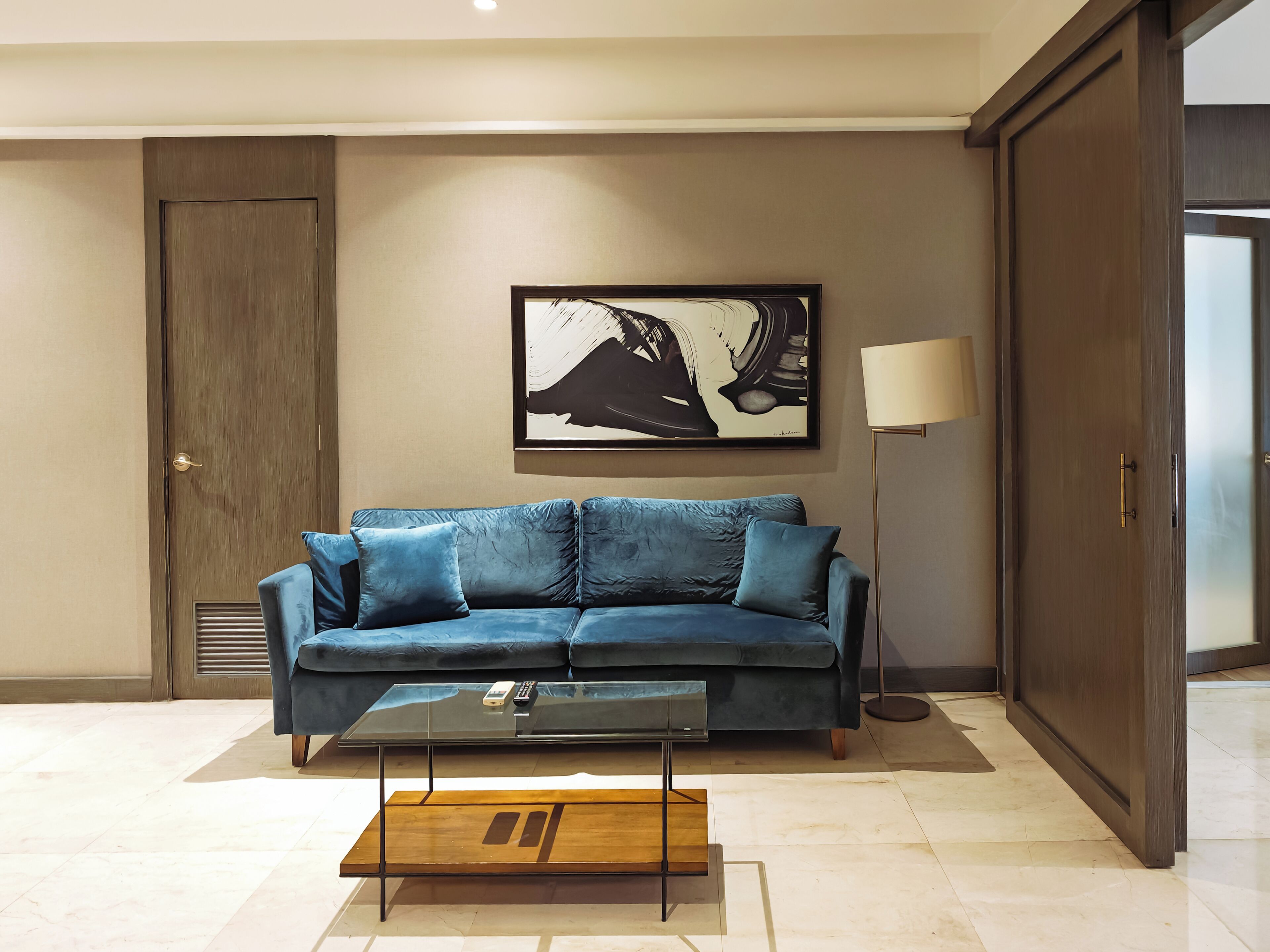 A modern living room with a blue sofa, a glass coffee table, and a framed artwork on the wall.