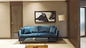 A modern living room with a blue sofa, a glass coffee table, and a framed artwork on the wall.