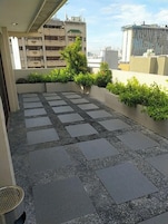 A rooftop terrace with a patterned stone floor, a small planter with greenery, and a view of surrounding buildings.