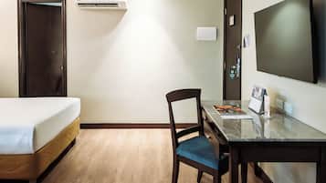 A hotel room with a bed, a desk, a chair, a flat-screen TV, and an air conditioning unit.