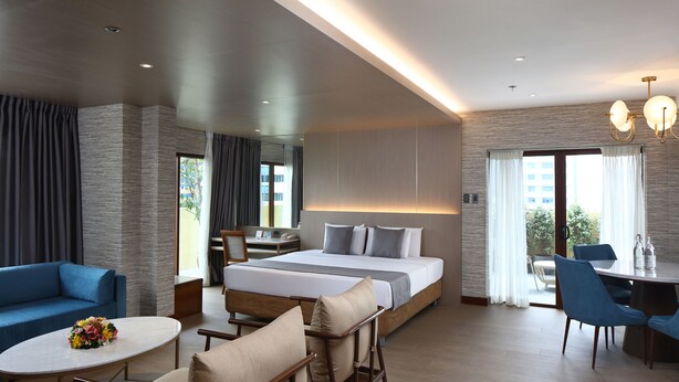 A modern hotel room with a large bed, a sitting area with a table and chairs, a desk, and a balcony with a view. - City Garden Suites Manila (Manila)