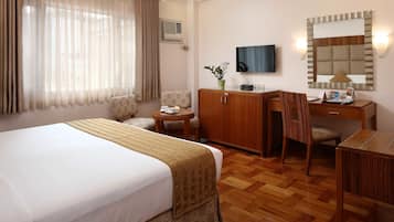 A hotel room with a large bed, a wooden desk, a chair, a television, and a mirror.