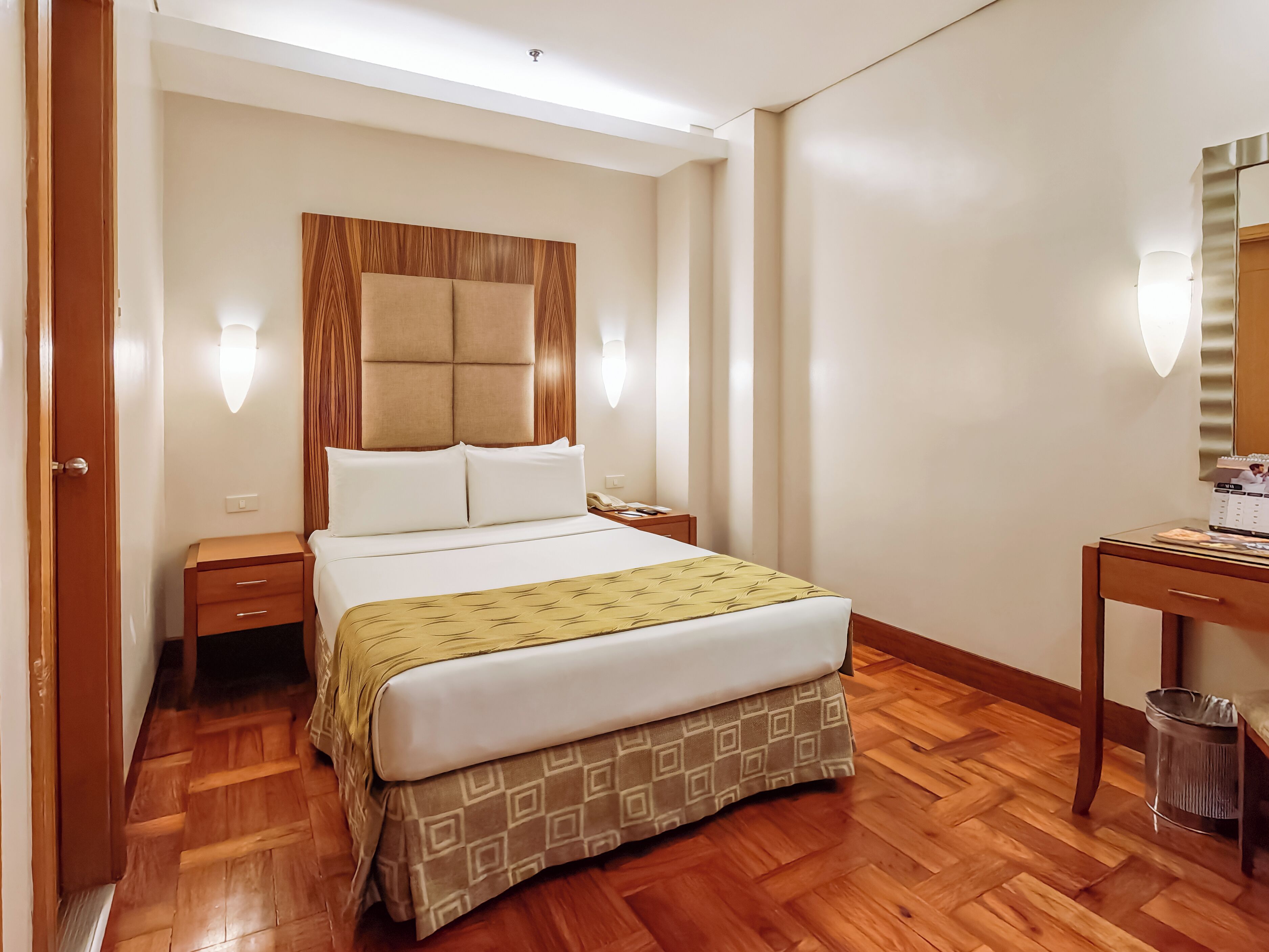 A hotel room with a bed, bedside tables, a desk, and a trash bin.