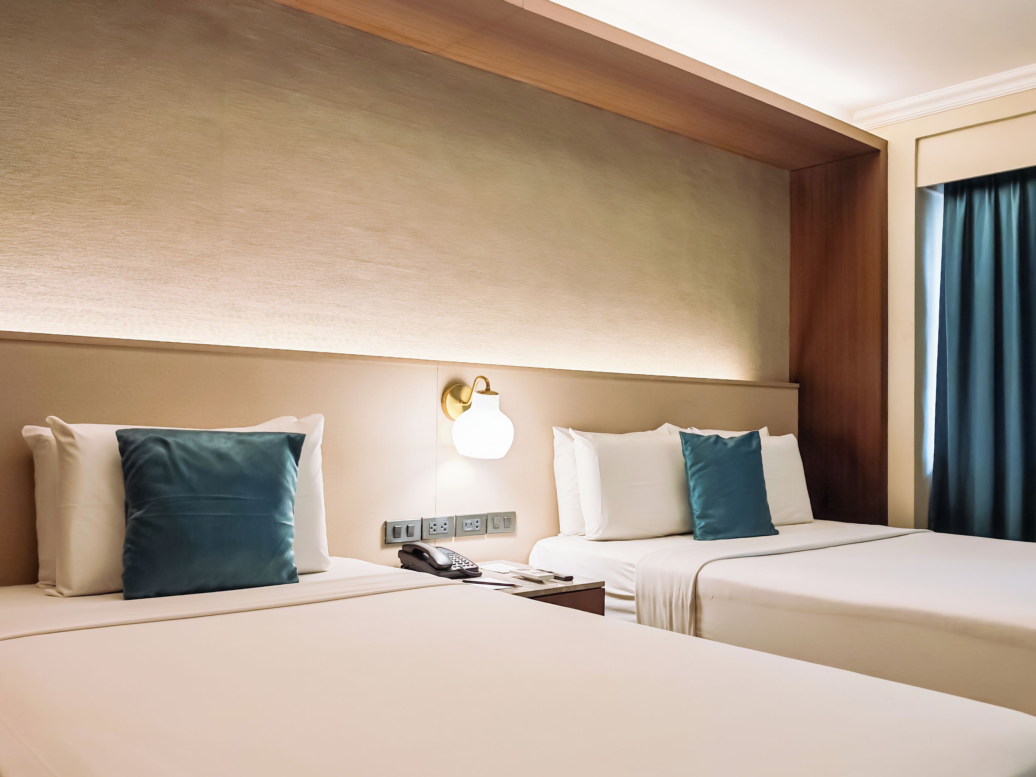 Une chambre d’hôtel avec deux lits, une table de chevet avec un téléphone et un luminaire fixé au mur.