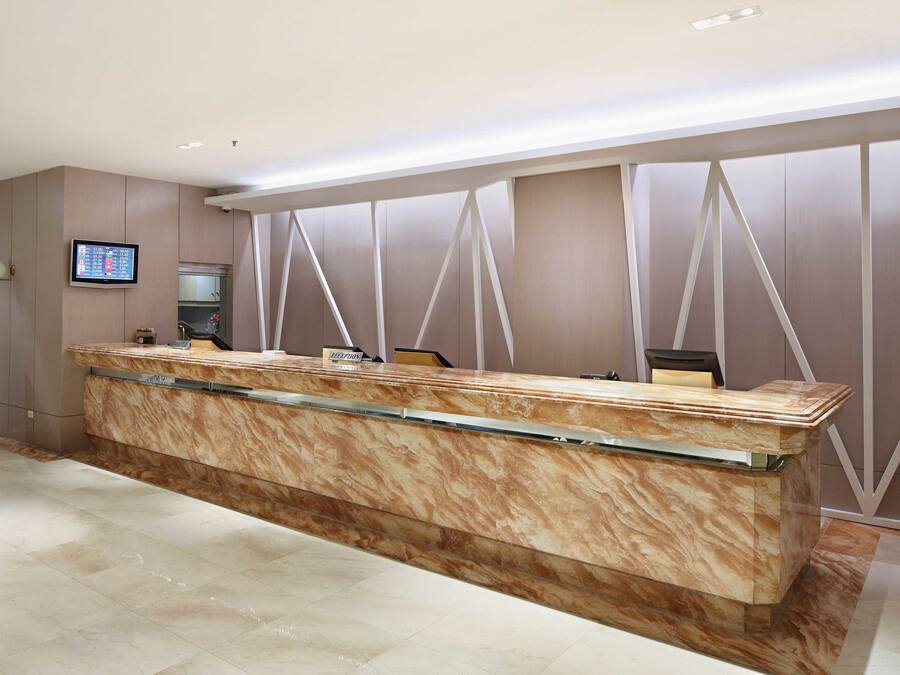 A reception desk with a marble top and glass panel, a digital screen, and a chair.