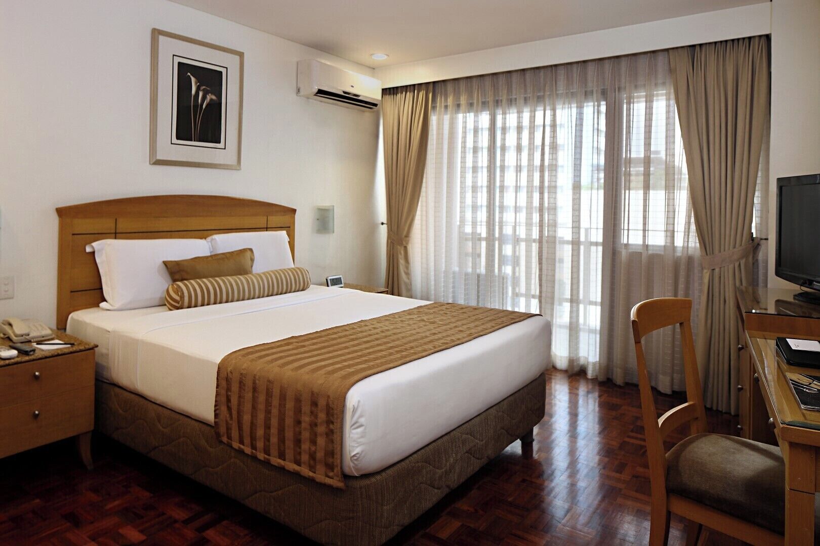 A hotel room with a bed, a desk with a chair, a television, and a window with curtains.