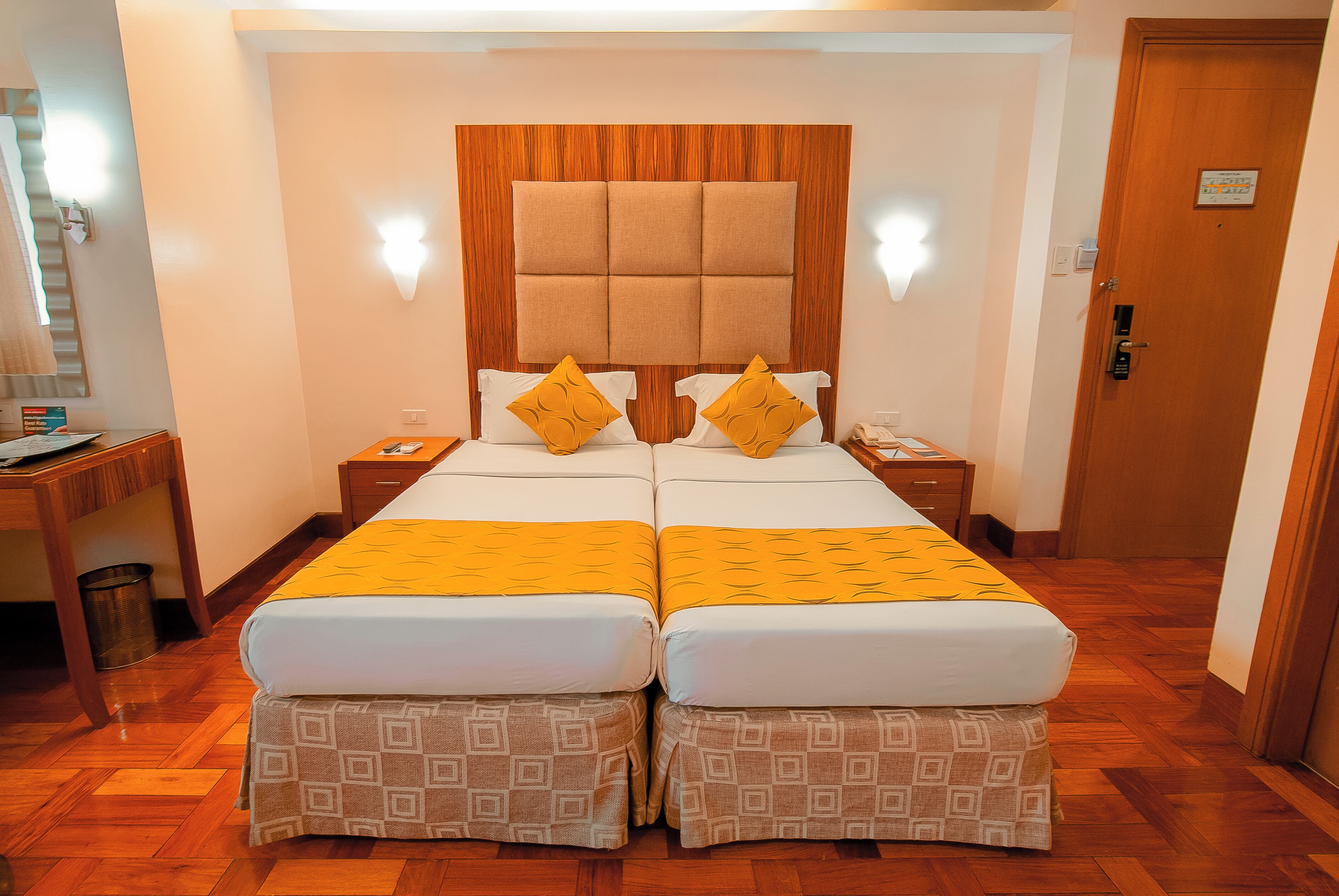 Uma cama de casal com cabeceira de madeira, duas mesas de cabeceira e um cobertor estampado.