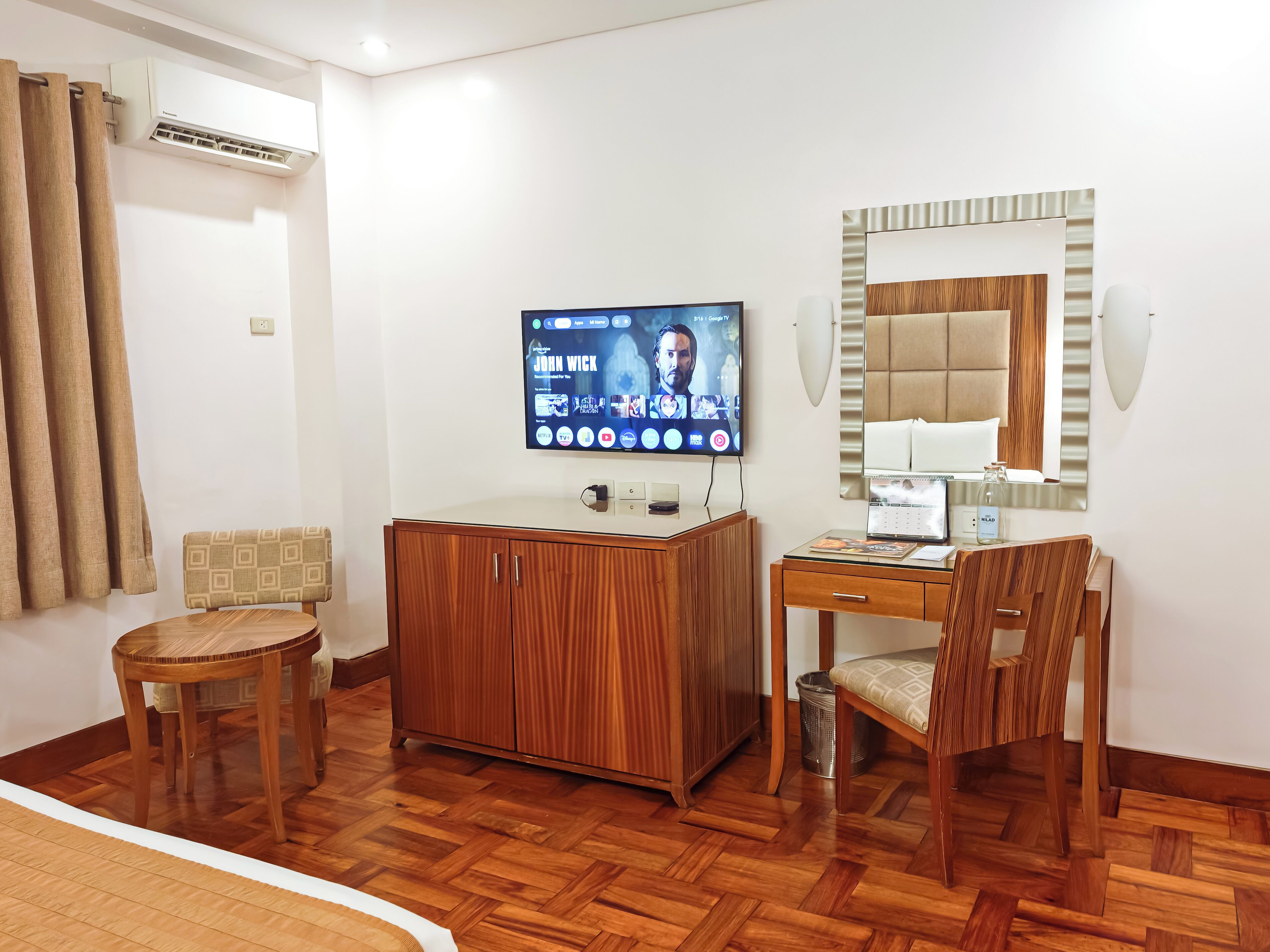 A hotel room with a wooden cabinet, a television, a desk with a chair, and a bed.