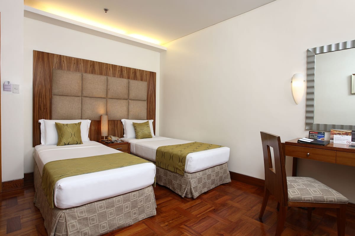A hotel room with two beds, a wooden headboard, a desk with a chair, and a mirror.