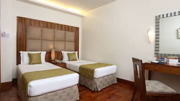 Quarto de hotel com duas camas, uma cabeceira de madeira, uma escrivaninha com cadeira e um espelho.
