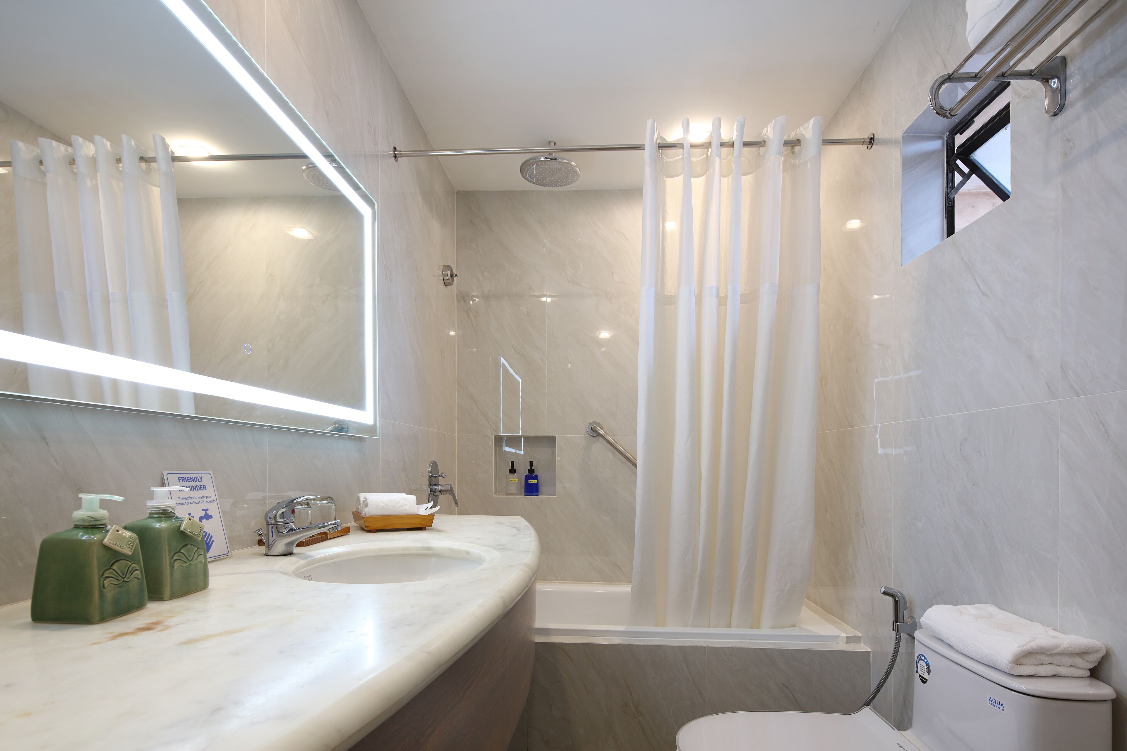 A modern bathroom with a marble sink, a large mirror, a shower with a curtain, and a toilet.