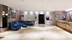 A modern lobby with a curved blue sofa, a reception desk, and a large potted plant. - City Garden Suites Manila (Manila)