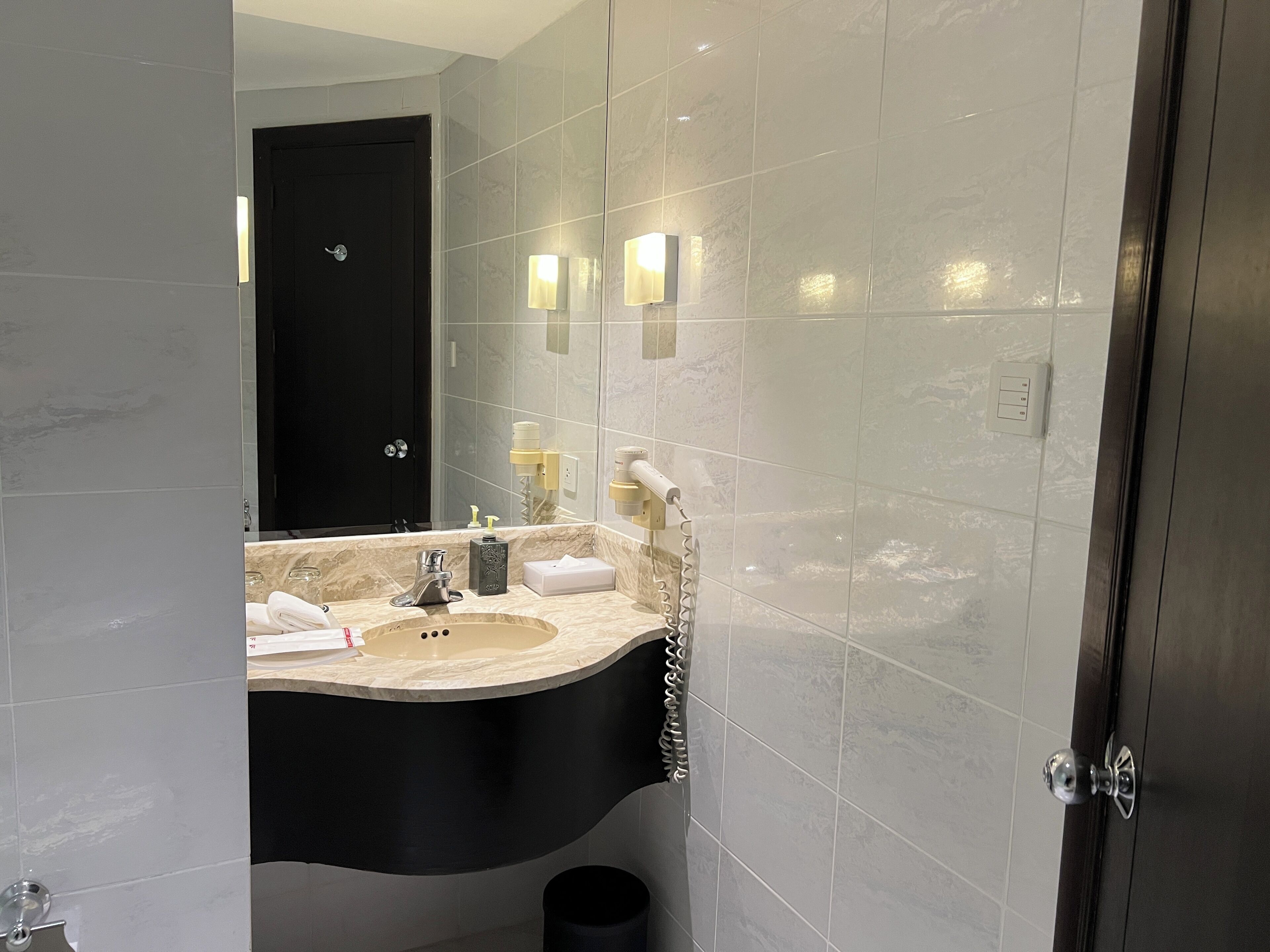 Un bagno moderno con un lavandino curvo, una porta scura e uno specchio che riflette l'ambiente.