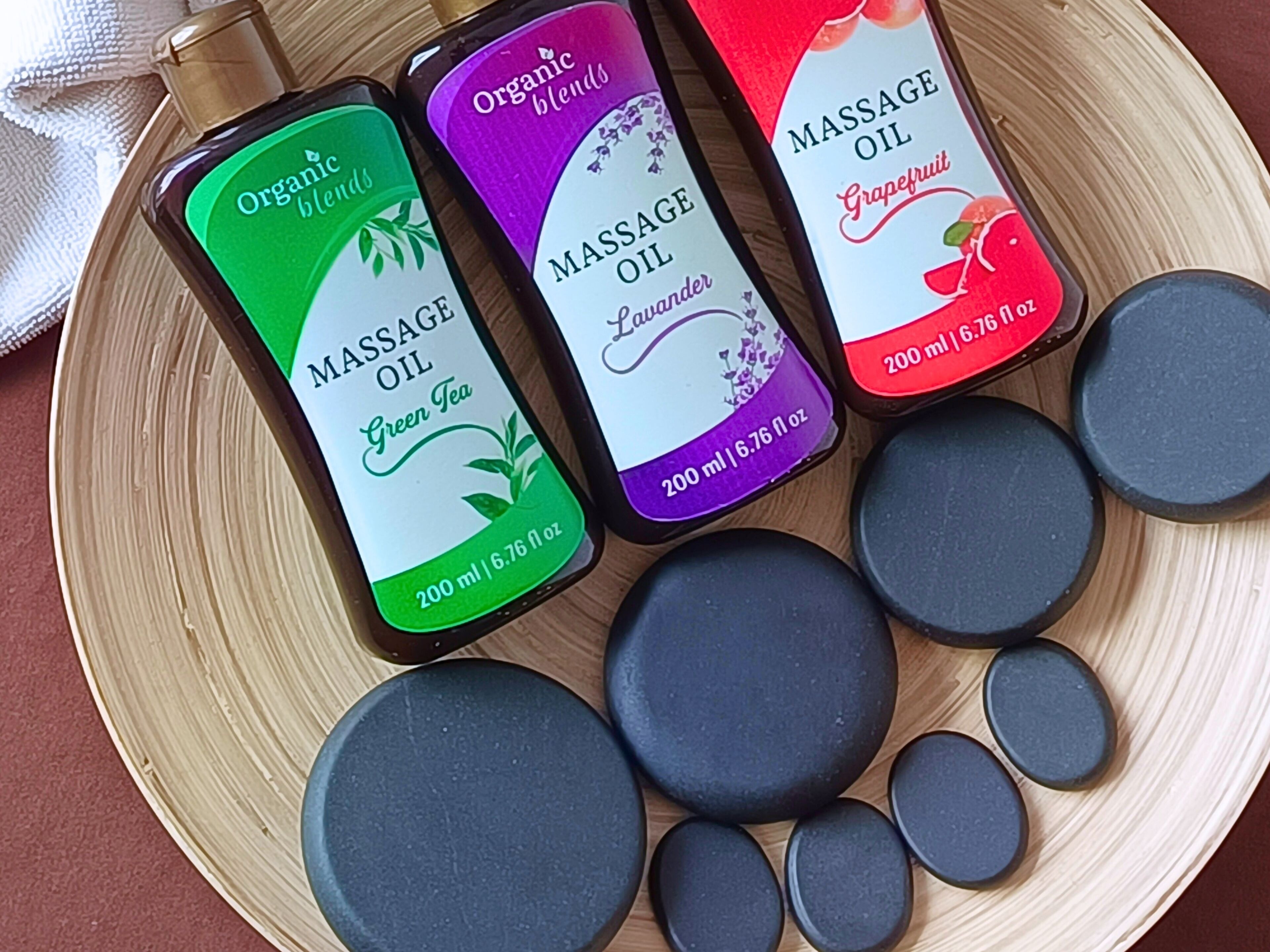 Three bottles of massage oil and several black stones on a wooden tray.