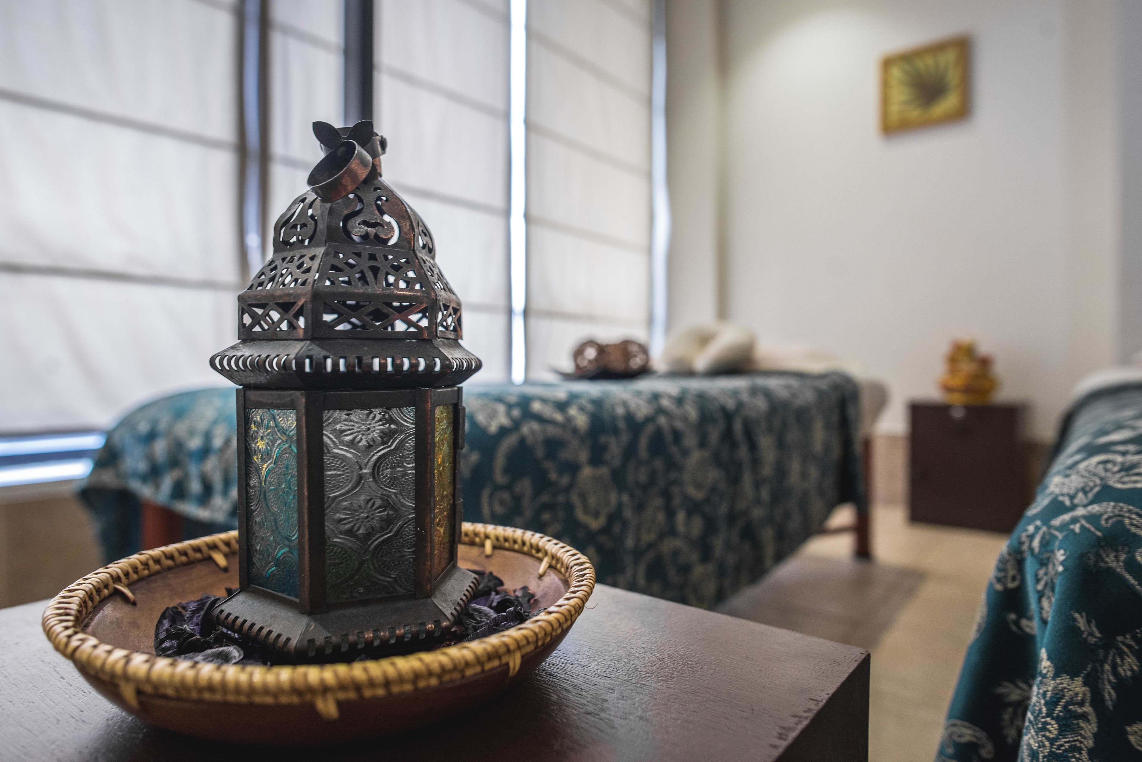 A room with a bed, a bedside table with a decorative lantern, and a window with blinds.