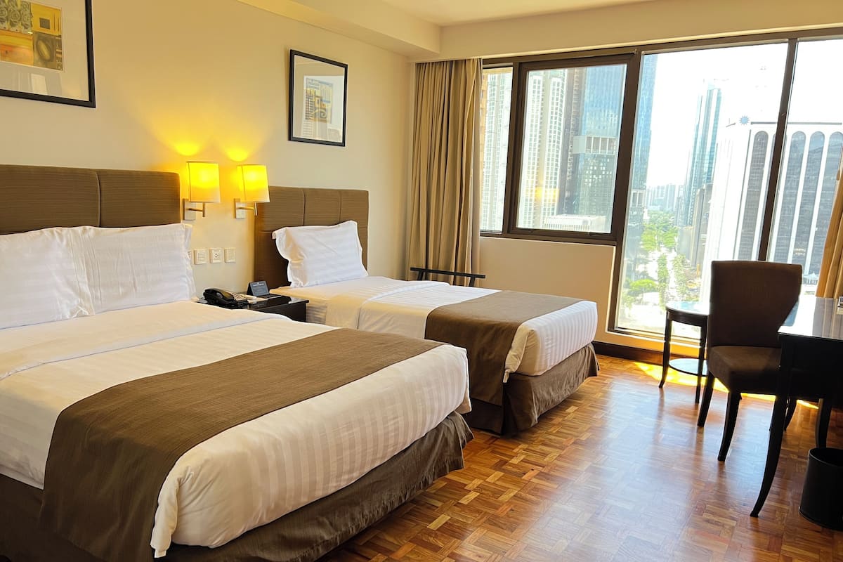 Habitación de hotel con dos camas, un escritorio, una silla y un ventanal con vista a la ciudad.